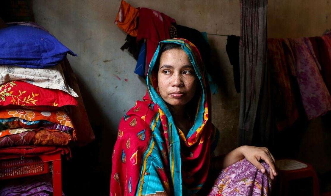 A woman sits in a dark room, looking beyond a pile of fabric