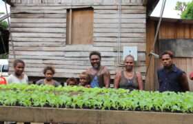 Family smiling behind plant boxes of crops they are growing