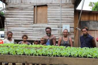 Family smiling behind plant boxes of crops they are growing