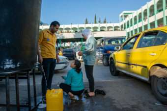 Mohammed and his two daughters are filling their containers with drinking water inside a government school in Deir al-Balah, a facility used as a shelter by Palestinians who have fled from the northern Gaza Strip.