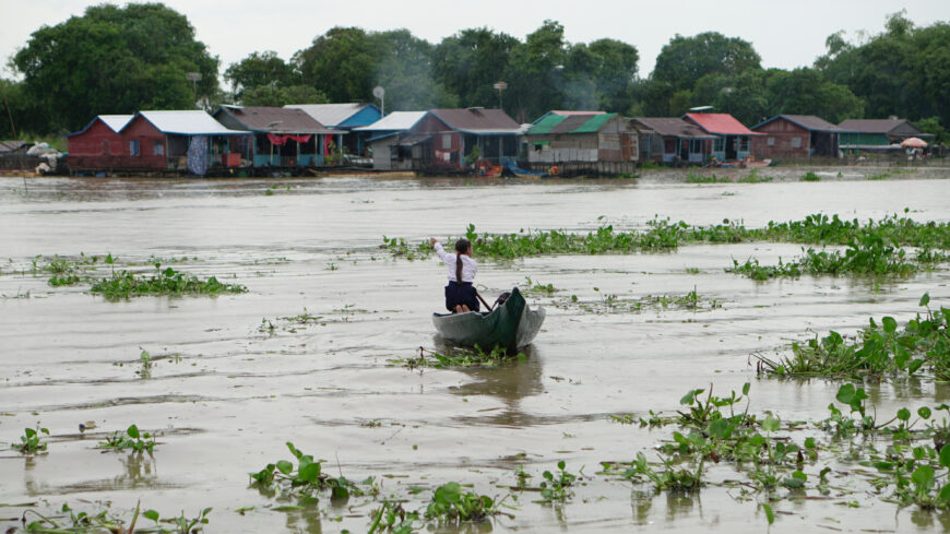 A child wearing a school uniform paddles a small boat across a flooded river to get to school