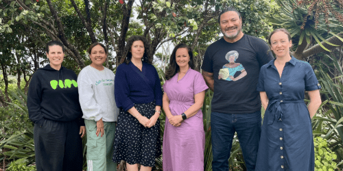 The six board of trustees stand in front of native bush in casual clothing.