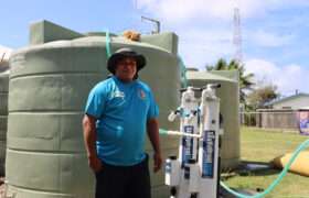 Tongan man smiling in front of water filter tank