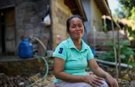 Lao woman in front of damaged home post flash floods.