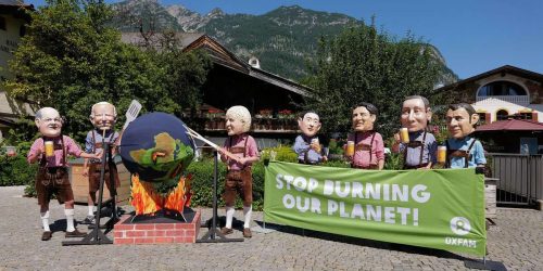 Climate Crisis Big Head Photo Stunt at Mohrenplatz, close to the Media Centre in Garmisch-Partenkirchen, Germany, 26.07.2022 
-.Oxfam campaigners pose as G7 leaders in Bavarian leather pants  roast the earth over a fireplace. Oxfam is calling on the G7 countries to commit to cutting emissions further and faster and provide more finance to help the most vulnerable countries respond to the impacts of climate change
-.G7 leaders in traditional Bavarian outfits (leather pants) standing at a fireplace and roasting the earth at a grill-spit. Behind them a banner demands: Stop burning our planet.